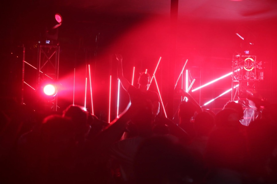 Crowd raising hands in red stage haze under vertical light bars at a night event in Jaipur