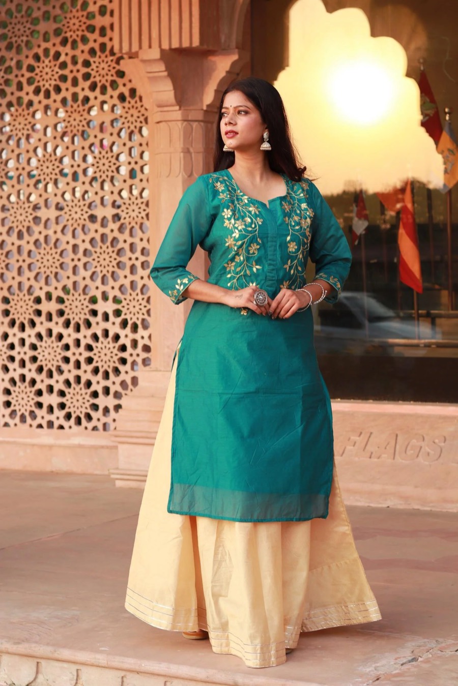 Teal embroidered kurta over a cream skirt, framed by a carved sandstone jali in warm sunlight