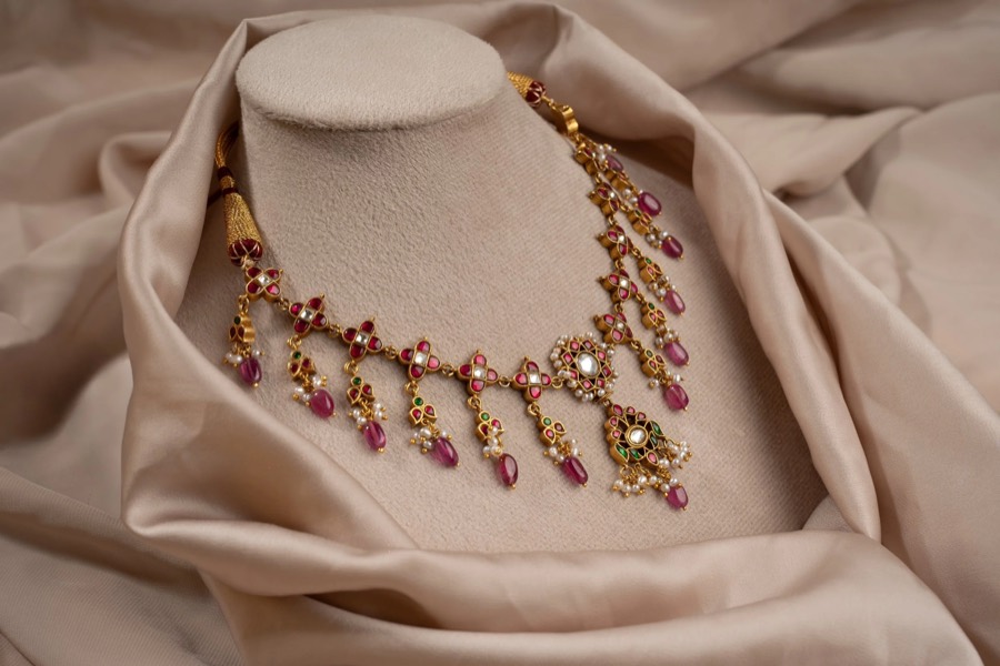 Gold necklace with pink teardrop danglers on a cream velvet bust, staged on champagne silk folds