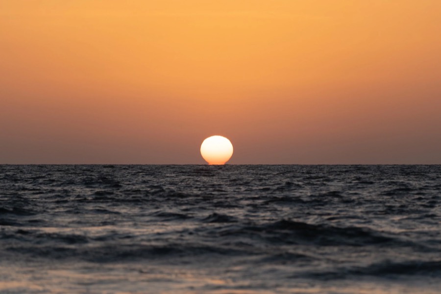Sun touching the horizon over the Arabian Sea off Goa, orange sky above dark rolling water