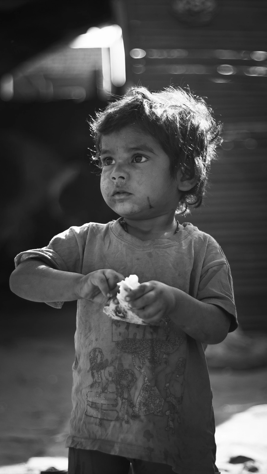 Small child holding a torn scrap of paper, printed tee, side light across a dark doorway behind