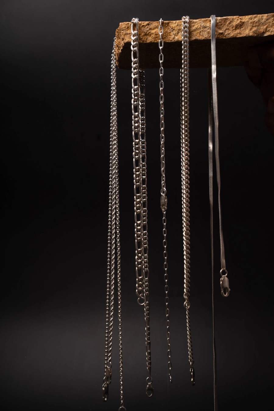 Silver chains hung in a row from a rough stone ledge, dark background isolating each link pattern