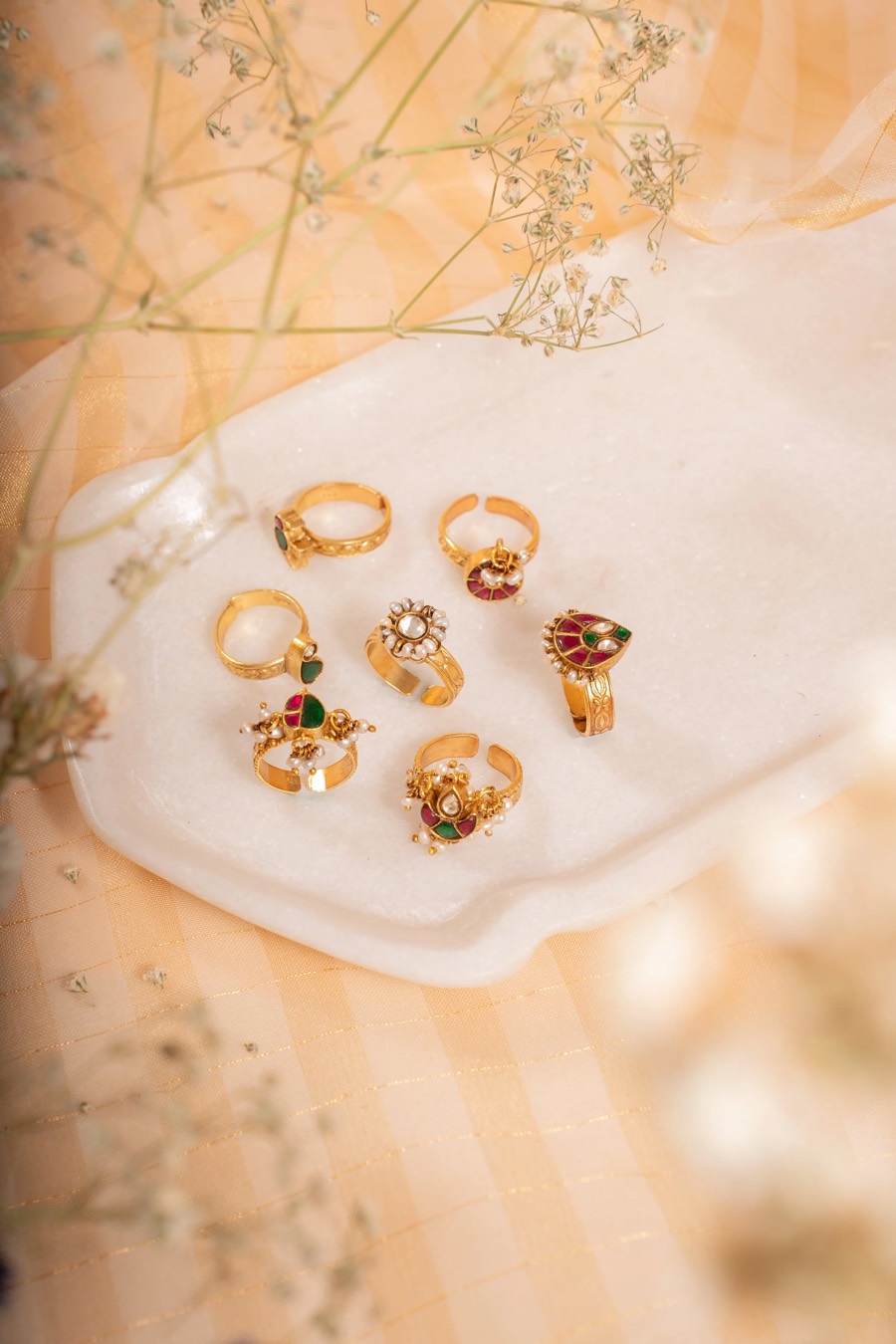 Seven gold rings laid out on a white tray, peach organza and baby's breath framing the flat-lay