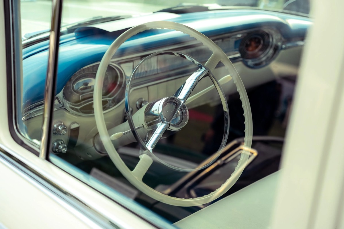 Ivory steering wheel and chrome horn ring seen through the open window of a blue and cream classic car