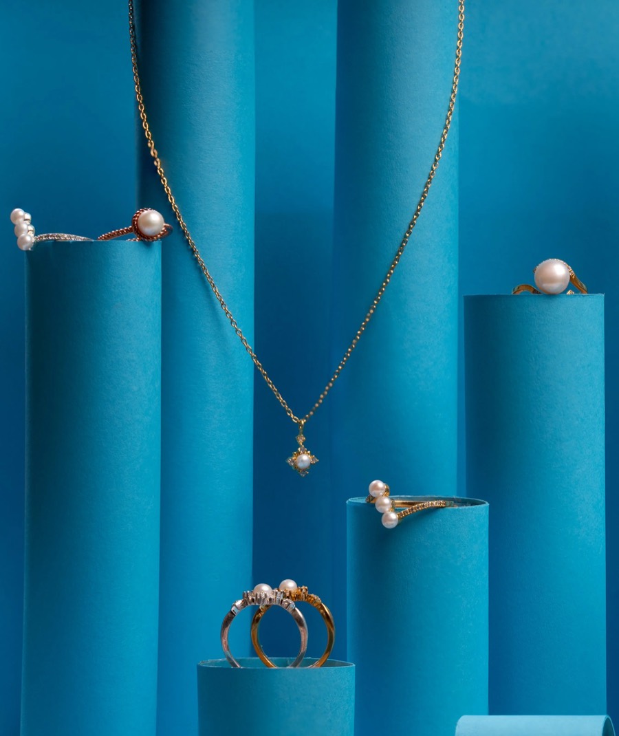Pearl rings and a gold pendant chain on teal paper cylinders — studio jewellery concept set-up