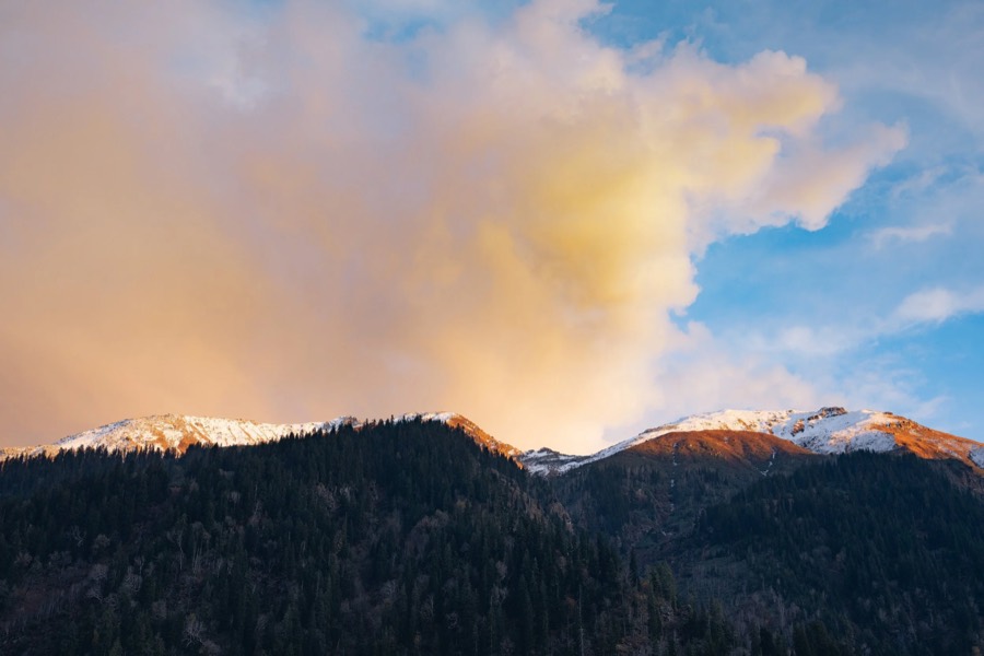 Sunset cloud burning orange above a dark forested crest, Waichin Valley, Himachal