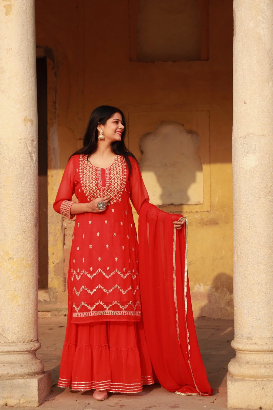 Red embroidered kurta and sharara with matching dupatta, styled against sandstone arches — Sutra