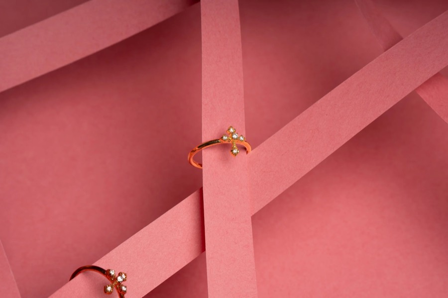 Two gold rings with tiny pearl clusters set on crossing dusty-pink paper bands, wide negative space