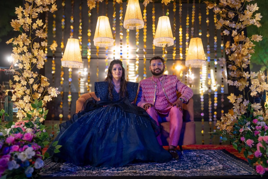 Reception stage seating, navy ball gown spread across a chair beside a pink striped jacket, lamps overhead
