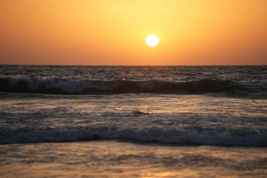 Golden sun hanging above lines of breaking surf rolling toward the shore at sunset in Goa