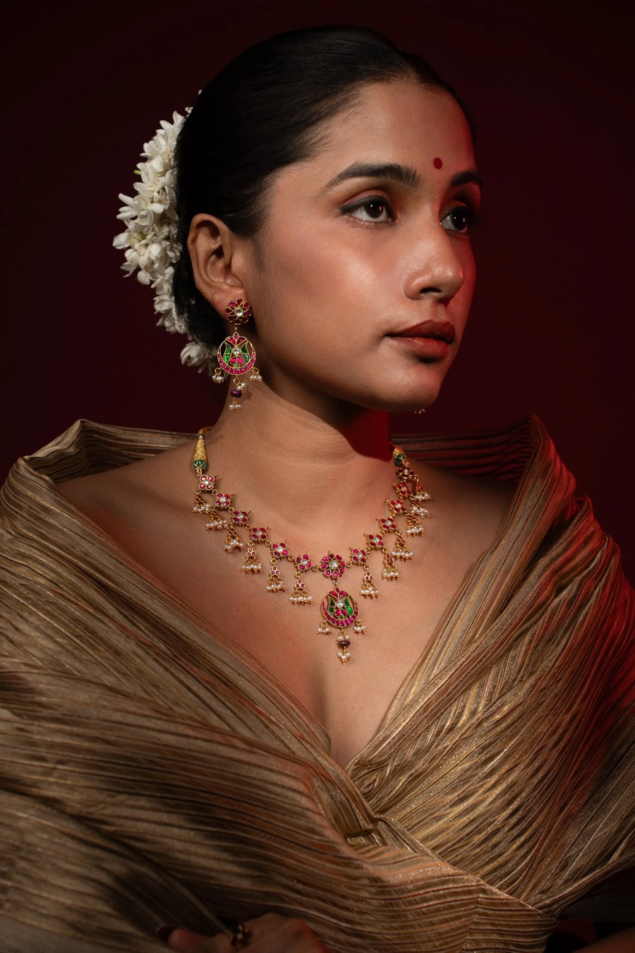 Model in a gold drape wearing a pink-stone Mahal Jewells necklace, jasmine gajra pinned in her bun