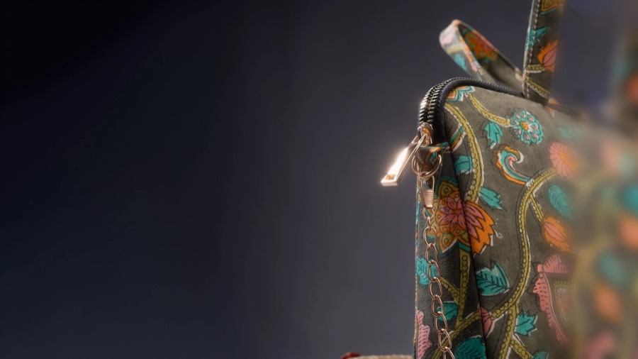 Close crop of an embroidered paisley handbag, the zip pull catching light against a dark backdrop