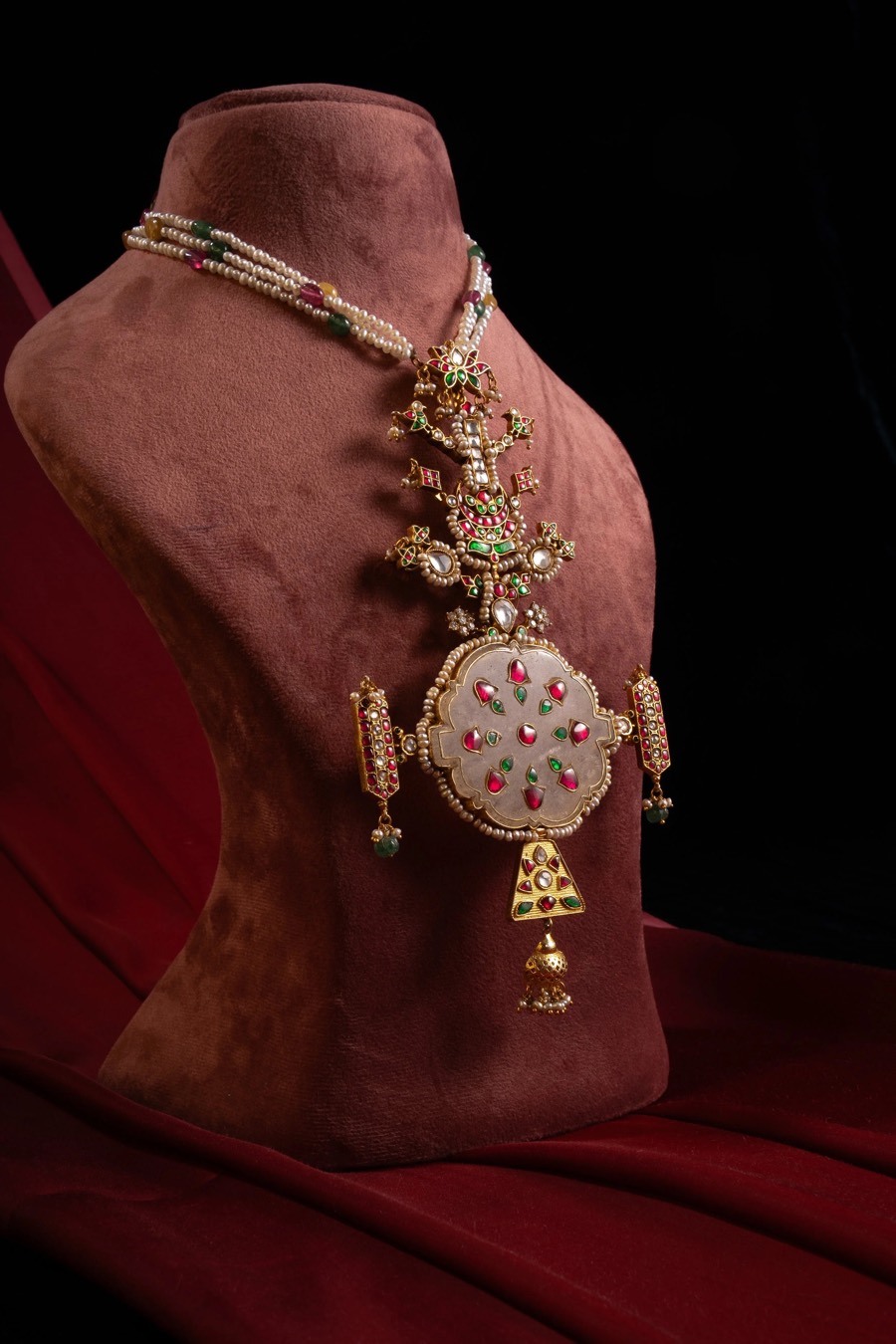 Long pendant haar on a rose velvet bust form, carved medallion and bell drop lit against black