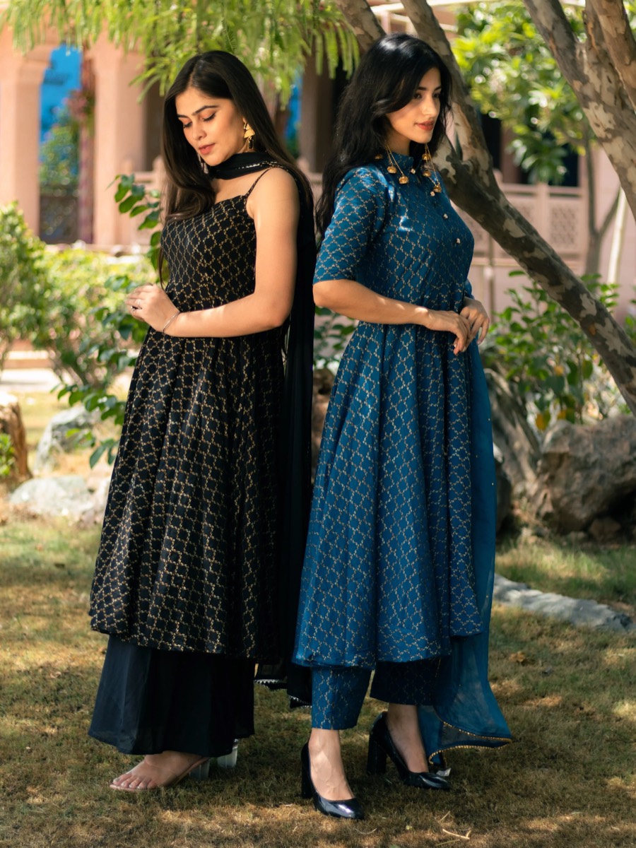 Two models in block-print anarkali sets, one black and one teal, on a sunlit garden lawn — Sutra
