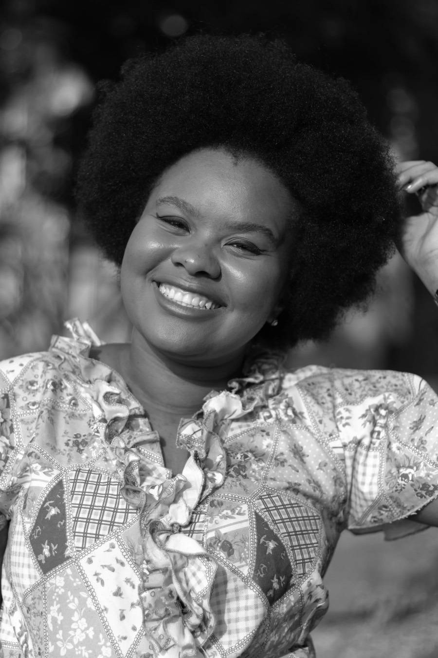 Outdoor black and white half-length, hand raised to voluminous curls, printed ruffled blouse, leaves behind