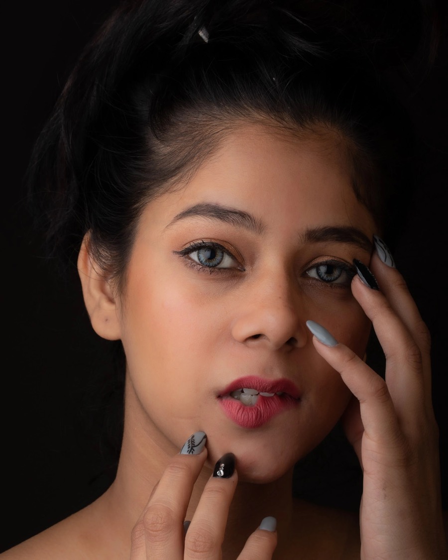 Beauty close-up against black, both hands framing the face, painted nails and sharp eyeliner in focus