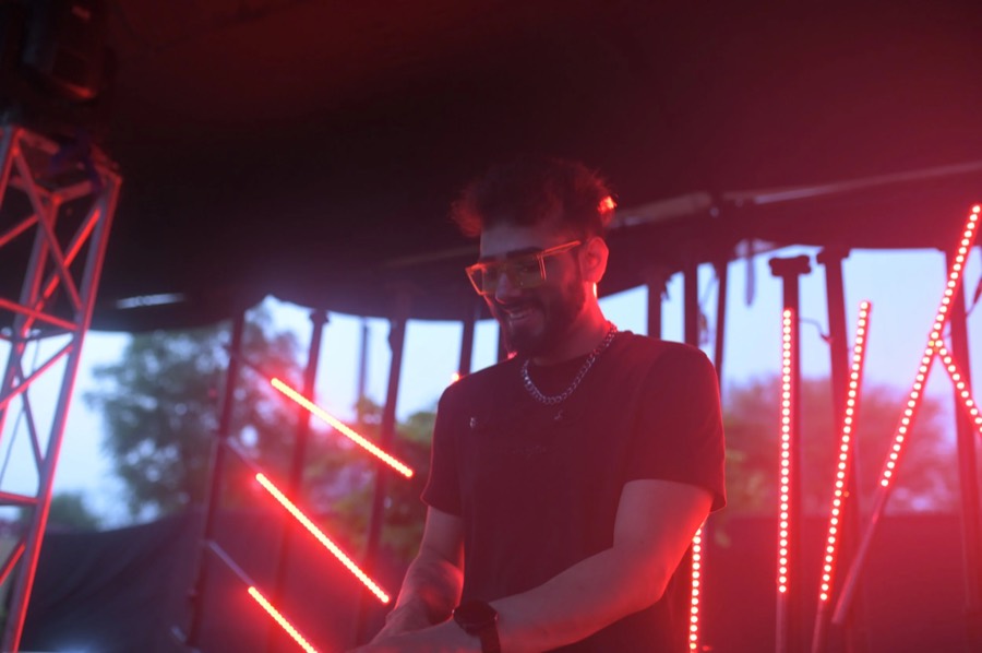 Performer in a black tee and sunglasses behind the decks, red LED strips glowing, Jaipur