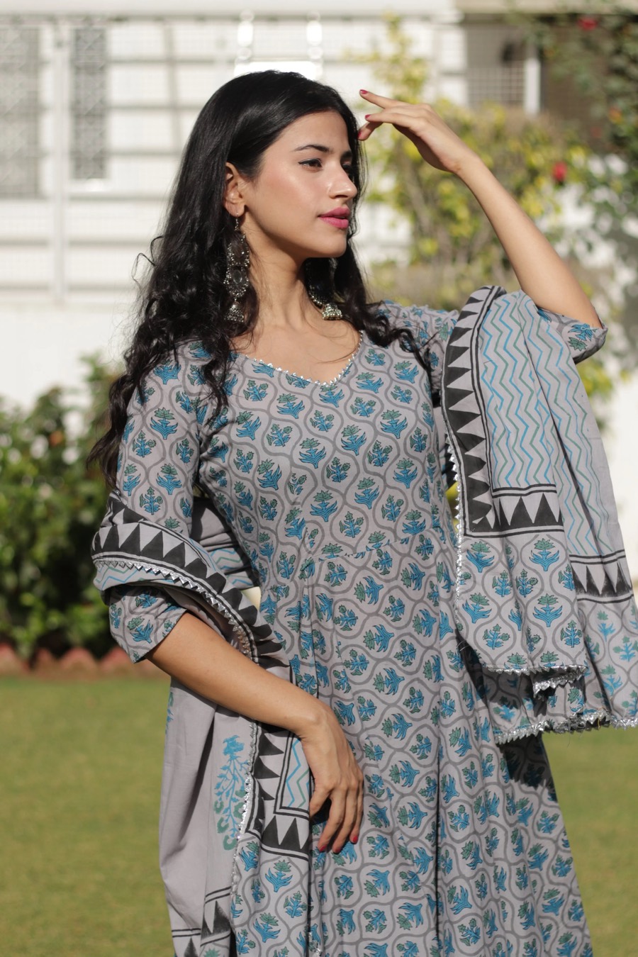 Grey and blue block-print anarkali with black borders, dupatta lifted mid-turn on a garden lawn