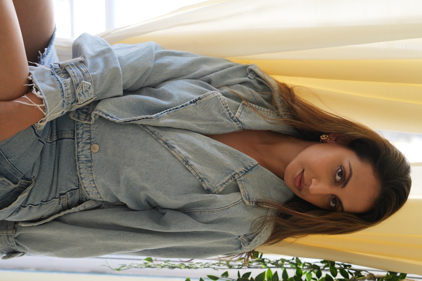 Fourth look: an oversized light-wash denim jacket and shorts, Anjali Schmuck against a yellow curtain