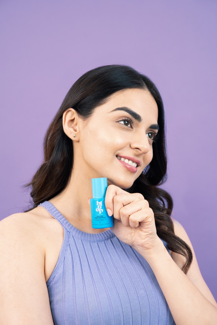 Ribbed lilac halter top, small cobalt serum bottle held at the chin, gaze off-camera on a purple sweep