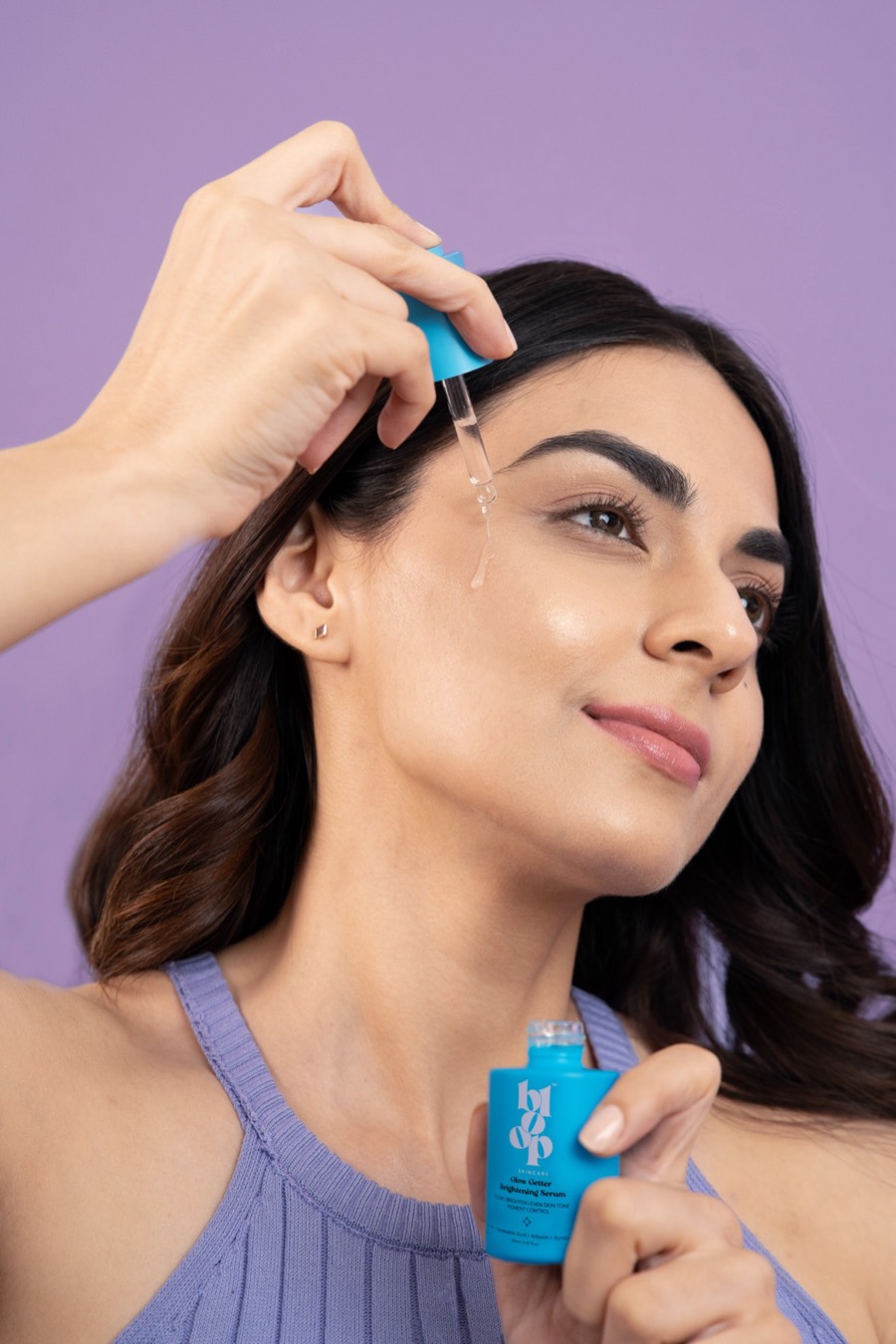 Dropper poised above the cheekbone, cobalt Bloop serum bottle in hand against a lilac backdrop