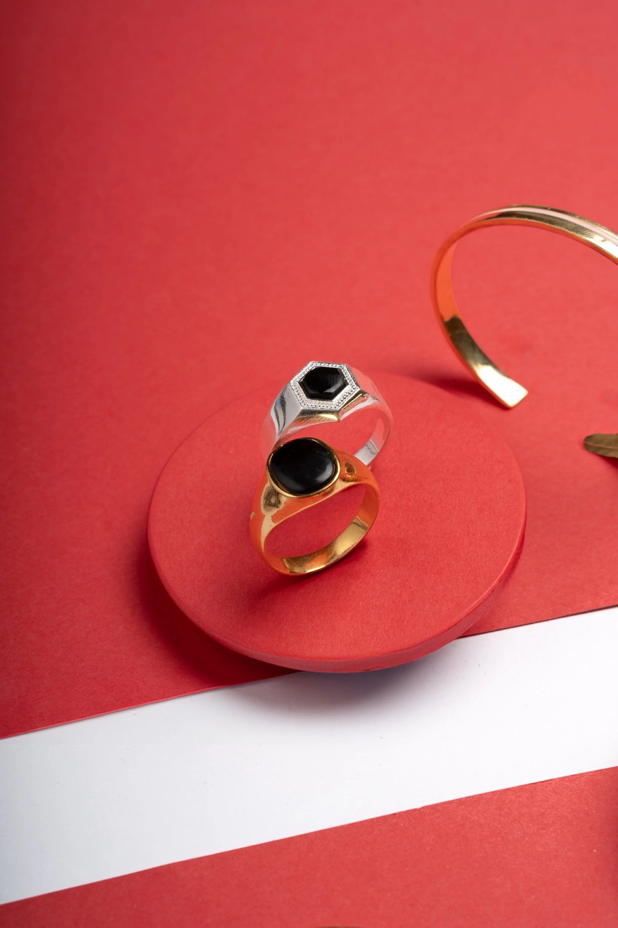 Silver and gold rings with black stones stacked on a red disc, a gold cuff curving behind