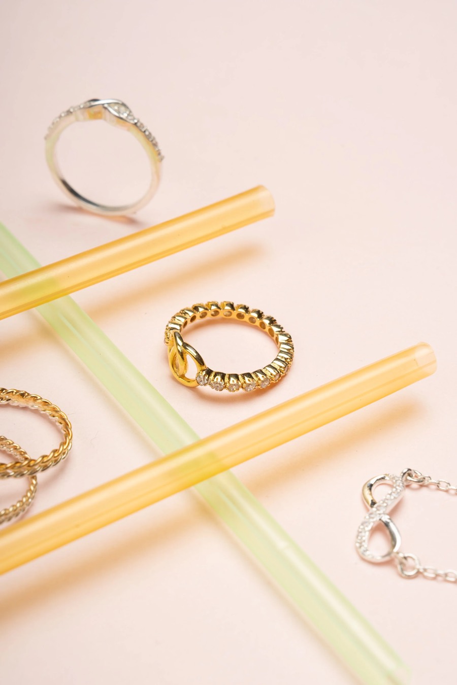 Twisted gold rope ring and stone-set bands among yellow and green translucent tubes on pale pink paper