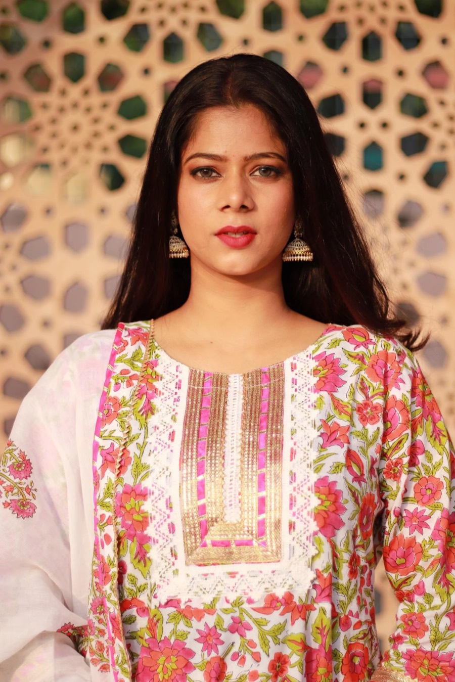 Close-up of a pink floral-print kurta with gold placket and jhumka earrings, jali screen behind