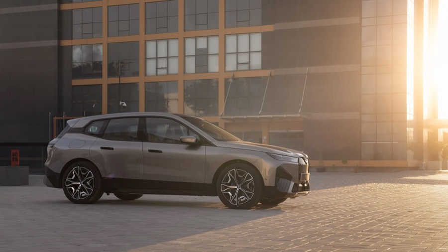 Silver crossover SUV parked side-on to a brick and glass building, low sun flaring past the roofline