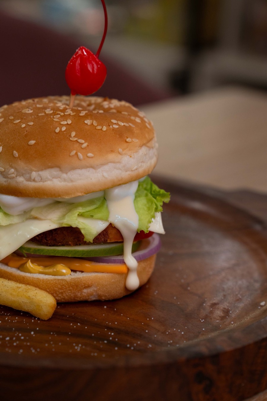 Sesame-bun burger stacked with lettuce, onion and dripping white sauce on a round wooden board