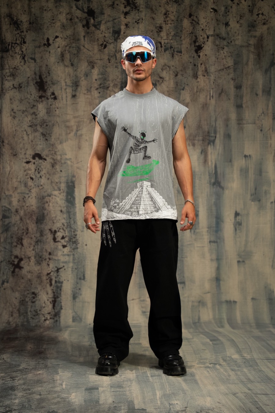 Full-length look: grey graphic sleeveless tee, white bandana and baggy black trousers on a grey set