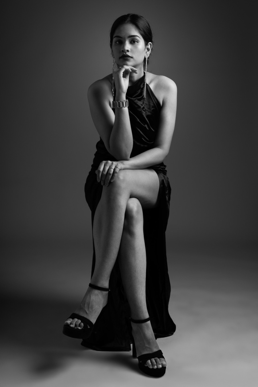 Hand at her chin on a studio stool, Shreya wears a black gown with a high slit, black and white