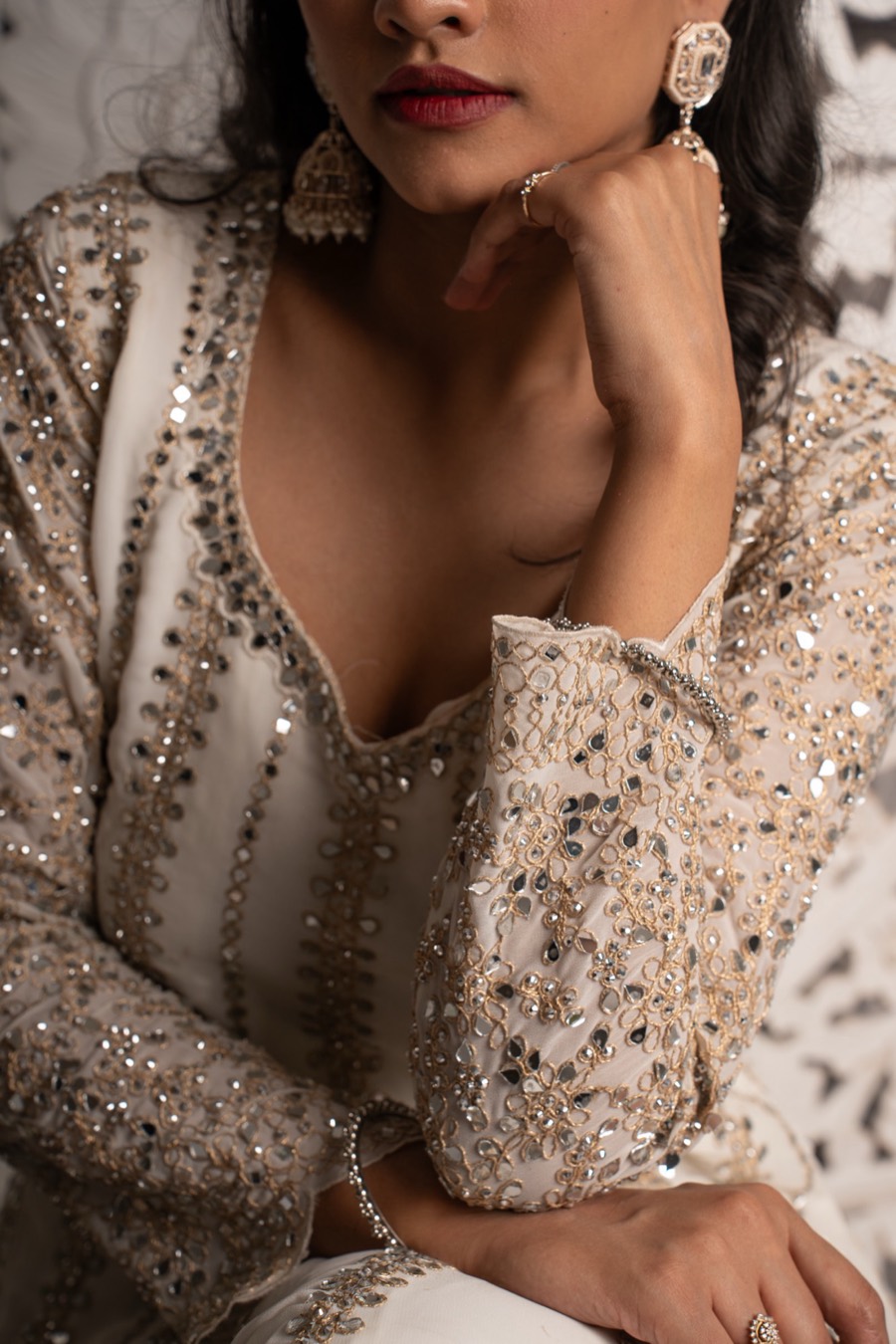Close crop on Shreya's ivory mirror-work outfit and drop earrings, hand lifted, frame cut at the lips